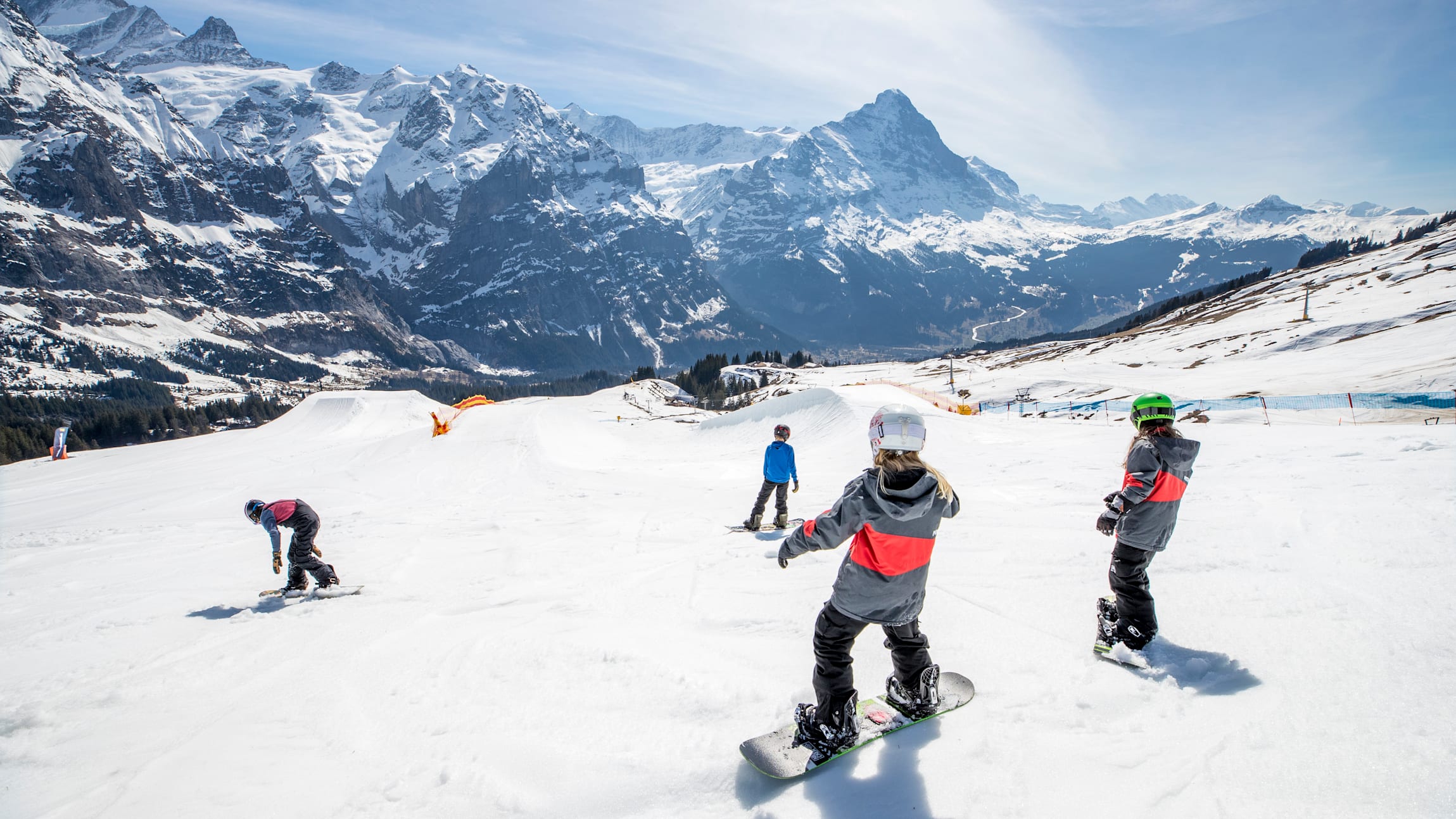 Snowpark Grindelwald First mit Kindern beim Snowboarden, Schnee und Berge sichtbar.