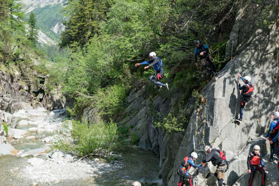 Grimsel Adventure Canyoning, participants jump from rocks, green surroundings, river in the background.