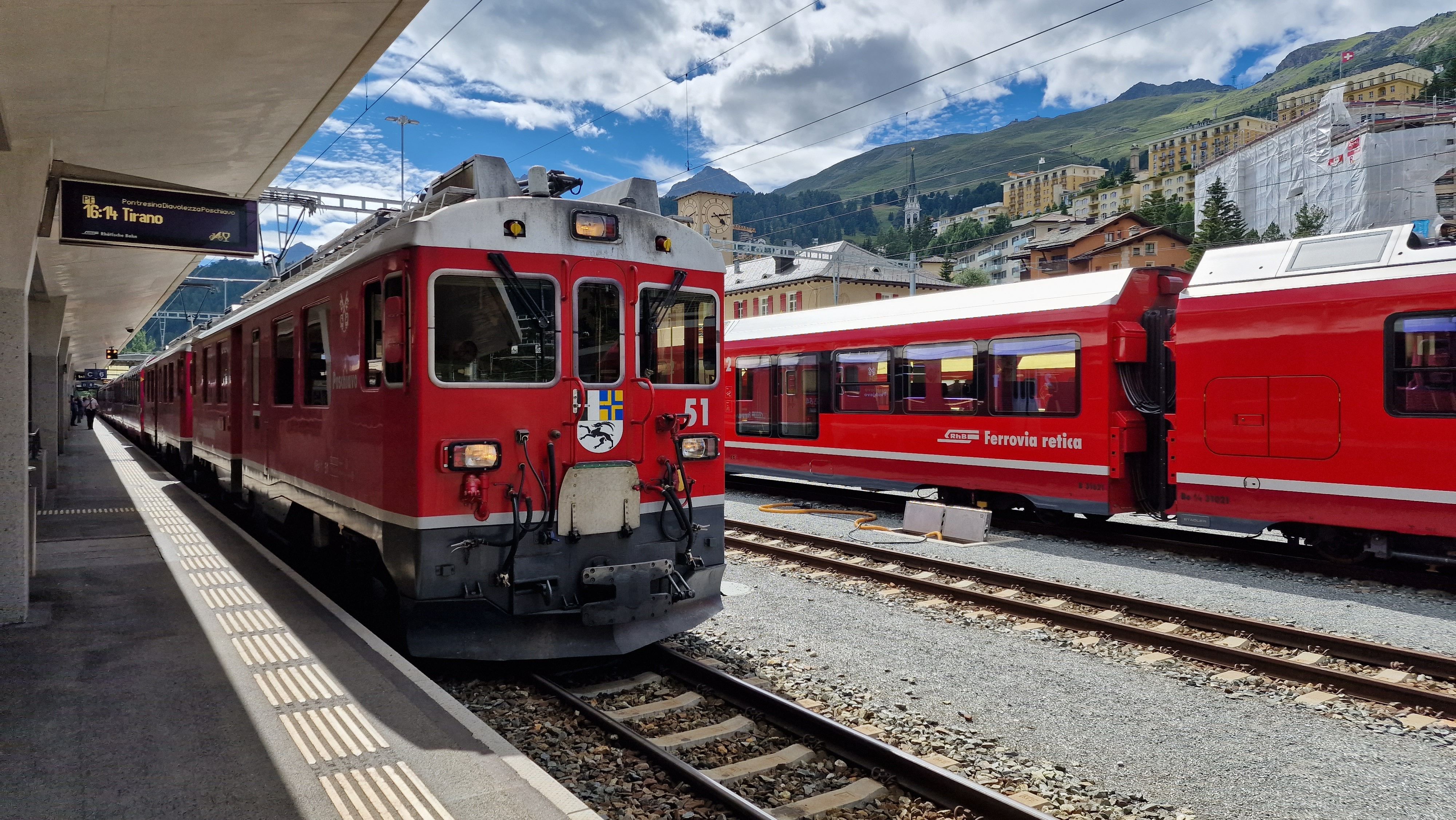 Ferrovie Retiche alla stazione di St. Moritz con impressionanti scenari montani e cielo sereno.