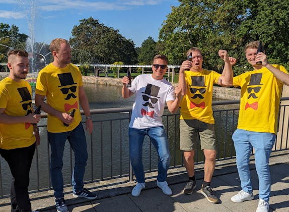 Derrota al Novio: Grupo en el evento de equipo festivo junto al lago con personas alegres en camisetas de colores.