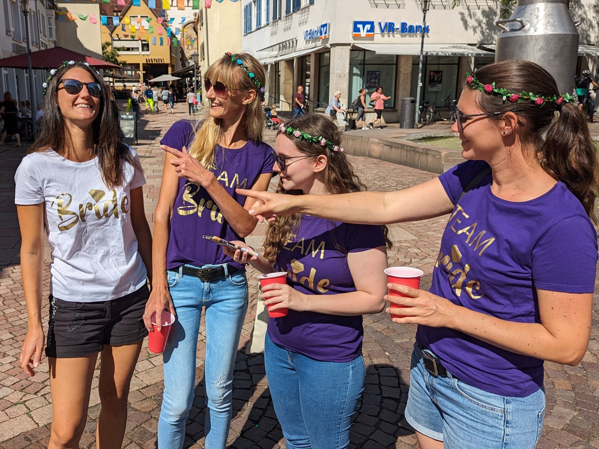 Equipo Novia: Grupo alegre en la ciudad con vasos rojo y blanco y coronas de flores. Fiesta divertida entre amigos.