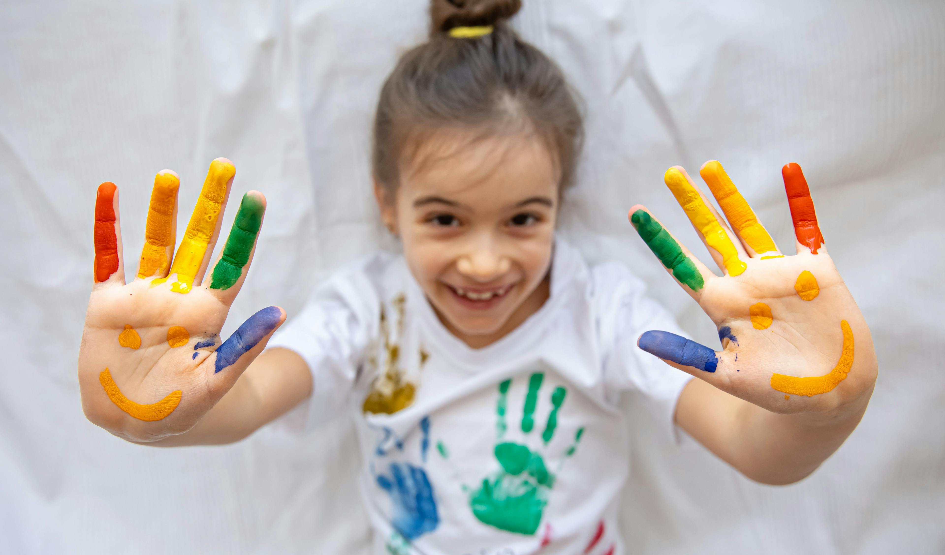 Painting on a T-shirt with colorful hands and the joyful facial features of a child.