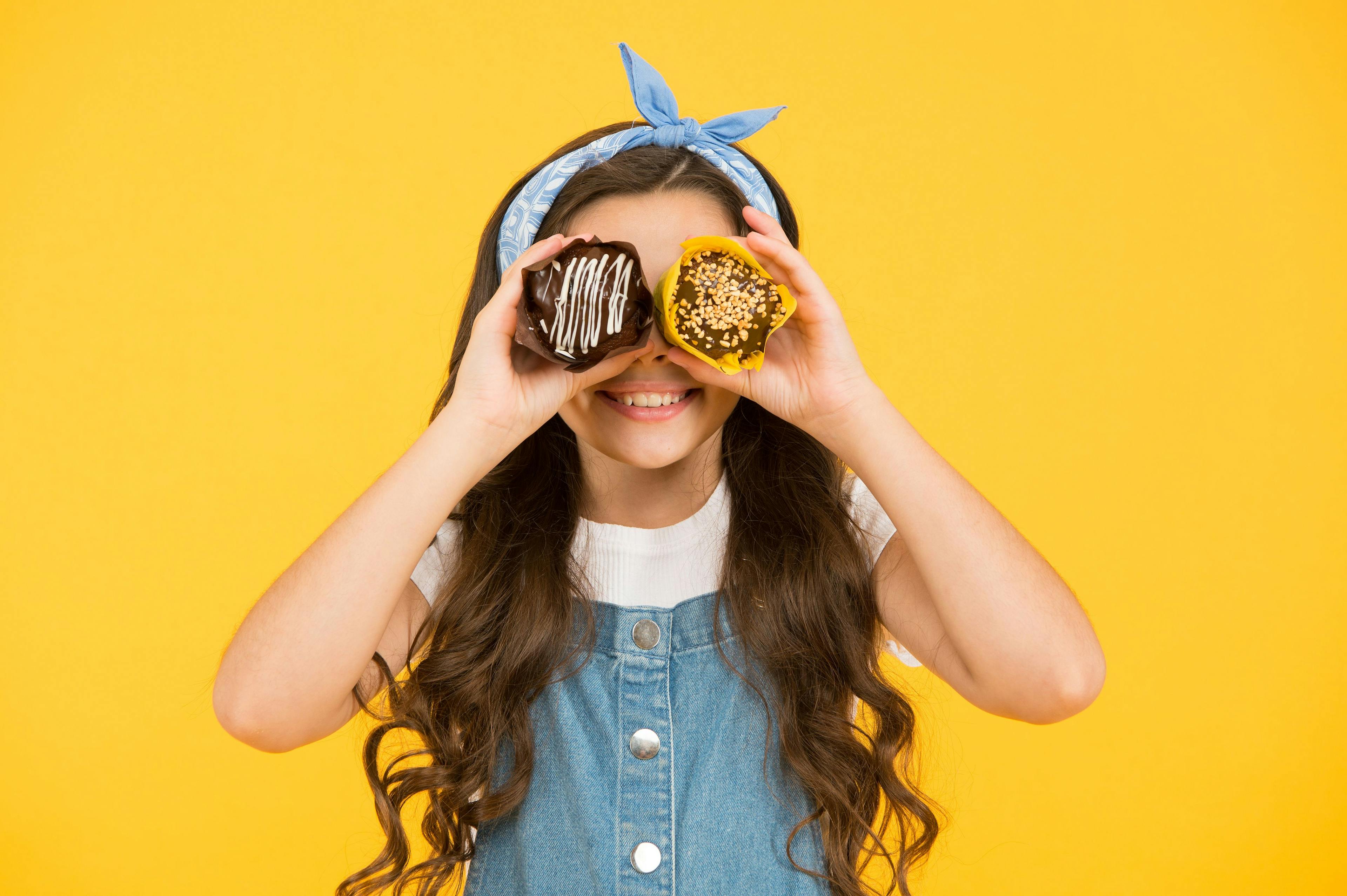 Bäckerei: Kind hält zwei leckere Donuts vor gelbem Hintergrund, ideal für süße Momente.