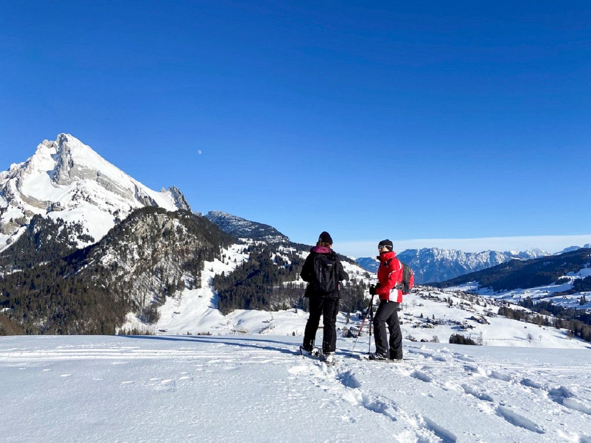 Schneeschuhwanderung in verschneiter Winterlandschaft mit Wanderern im Gespräch mit Bergen im Hintergrund.