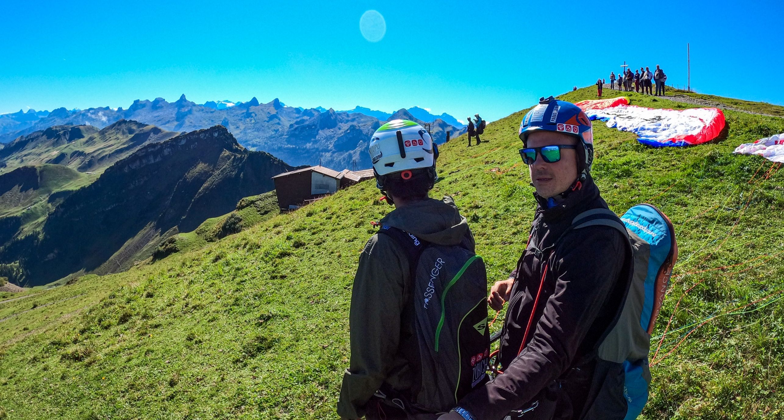 Volo in parapendio Fronalpstock con piloti, prato verde, cielo sereno.