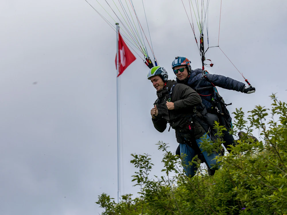 Paraglidning i Zurich med två piloter över gröna kullar.