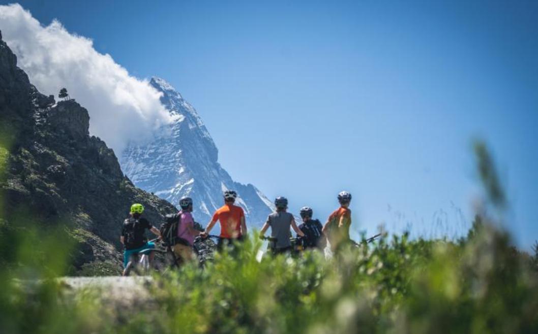 Perjalanan MTB dasar di Alpen bersama kelompok pesepeda di depan pegunungan yang megah.