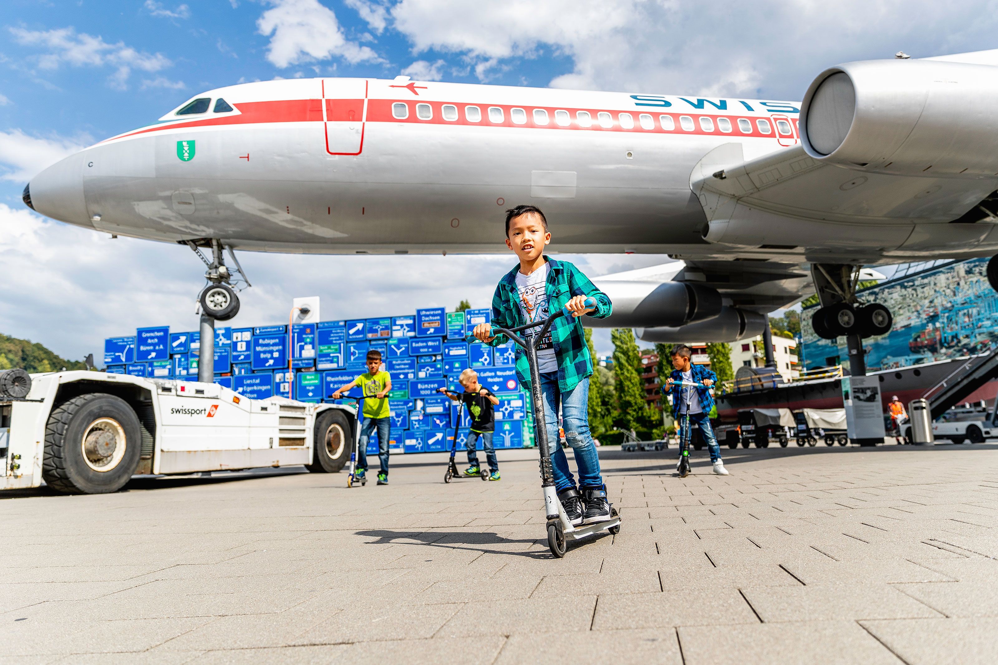 Παιδιά που οδηγούν πατίνια κοντά στο Μουσείο Μεταφορών του Λουσέρεν κάτω από μια αεροπορική πτήση