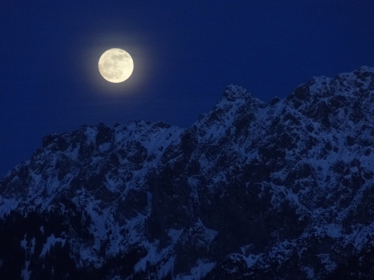 Snöskovandring: Fullmåne över snötäckta berg i vinterlandskap på natten.