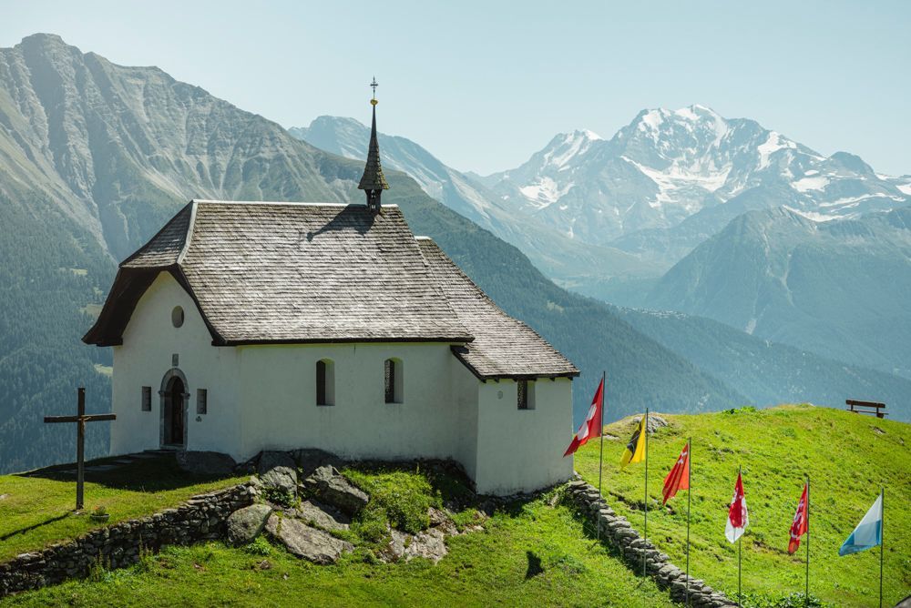 Arena Aletsch con capilla y montañas al fondo, senderismo en un día soleado de verano.