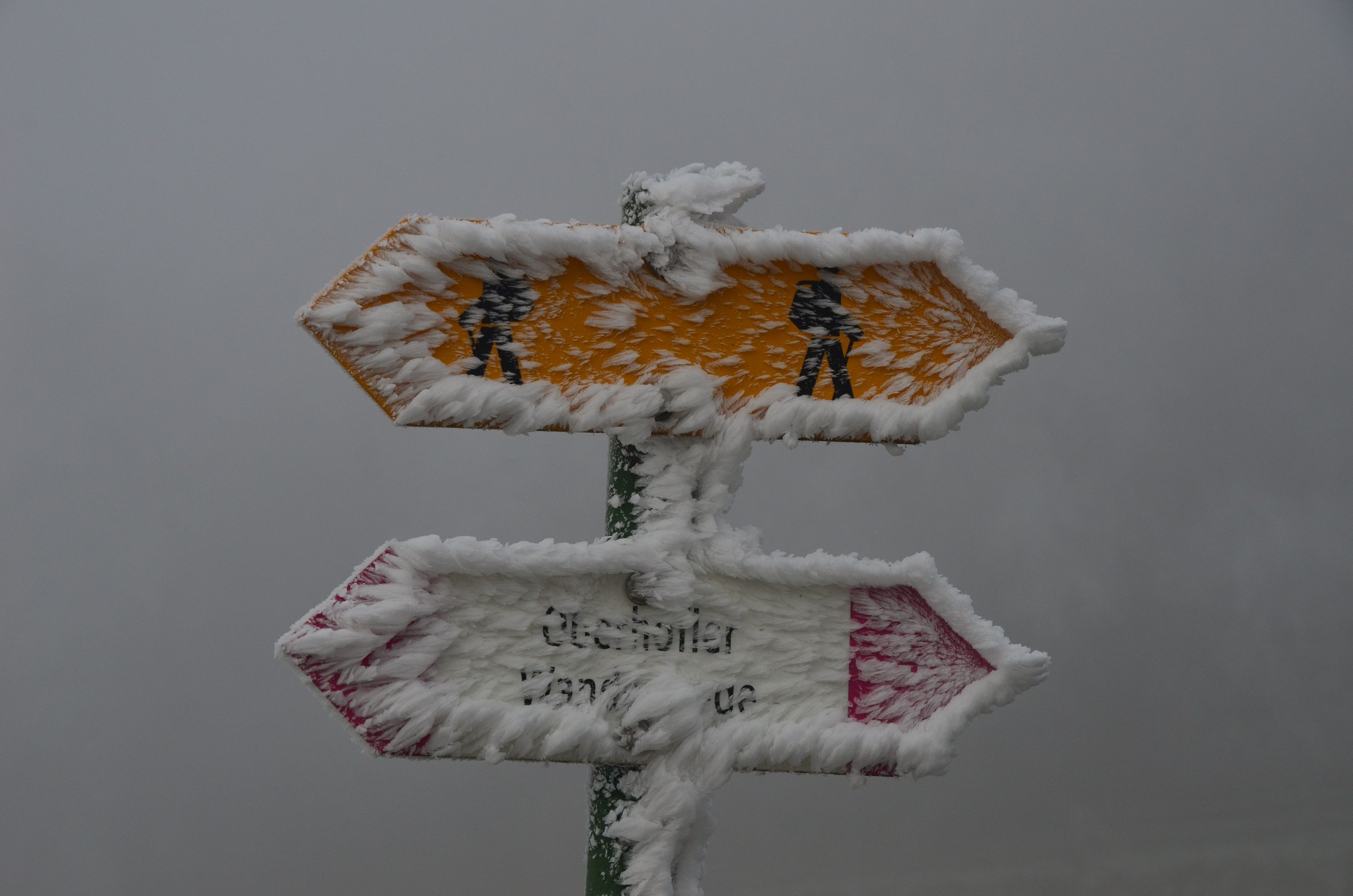 Winterwanderung: Wegweiser im Eis, zeigt traumhafte Wanderwege in den verschneiten Bergen.