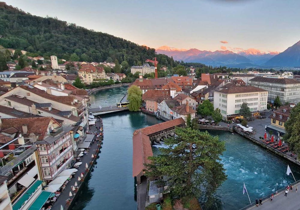 Thun: pitoresca paisagem urbana à beira do rio com edifícios históricos e montanhas ao fundo.