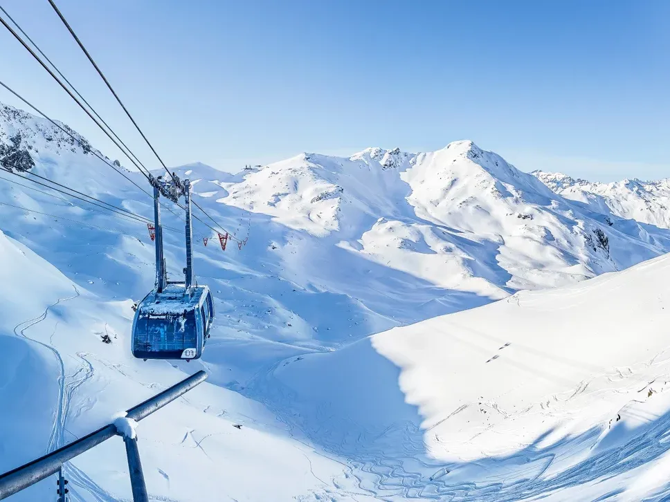 موقع أروس للتزلج مع التلفريك، جبال مغطاة بالثلوج وسماء زرقاء.