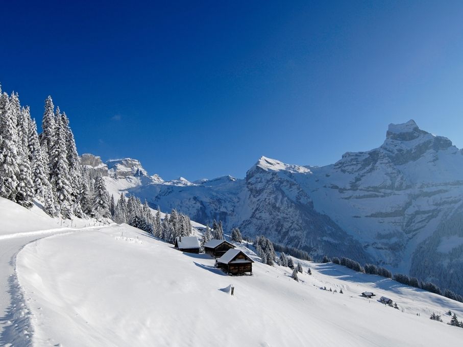 Inverno Brunni: Paesaggio coperto di neve con baite e montagne innevate al sole invernale.