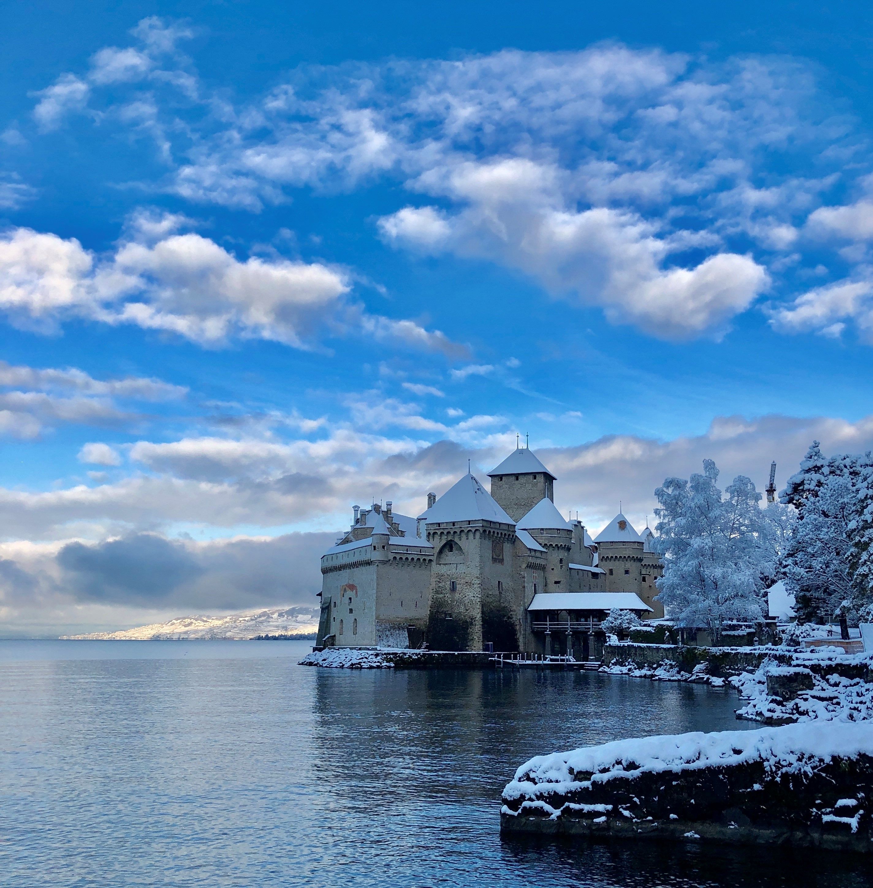 Chateau Chillon di Tasik Geneva semasa musim sejuk dengan salji dan gunung.