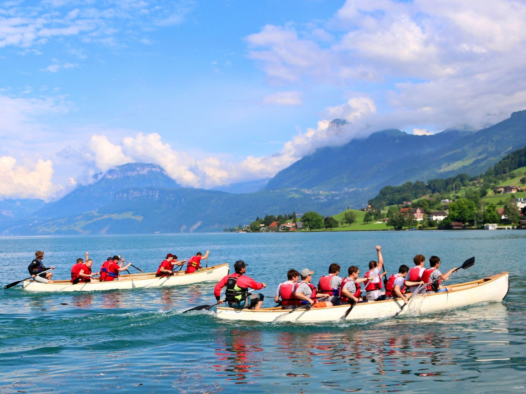 Husky kanadyjskie podczas wydarzenia zespołowego na Jeziorze Czterech Kantonów, otoczone górami i pełne akcji.