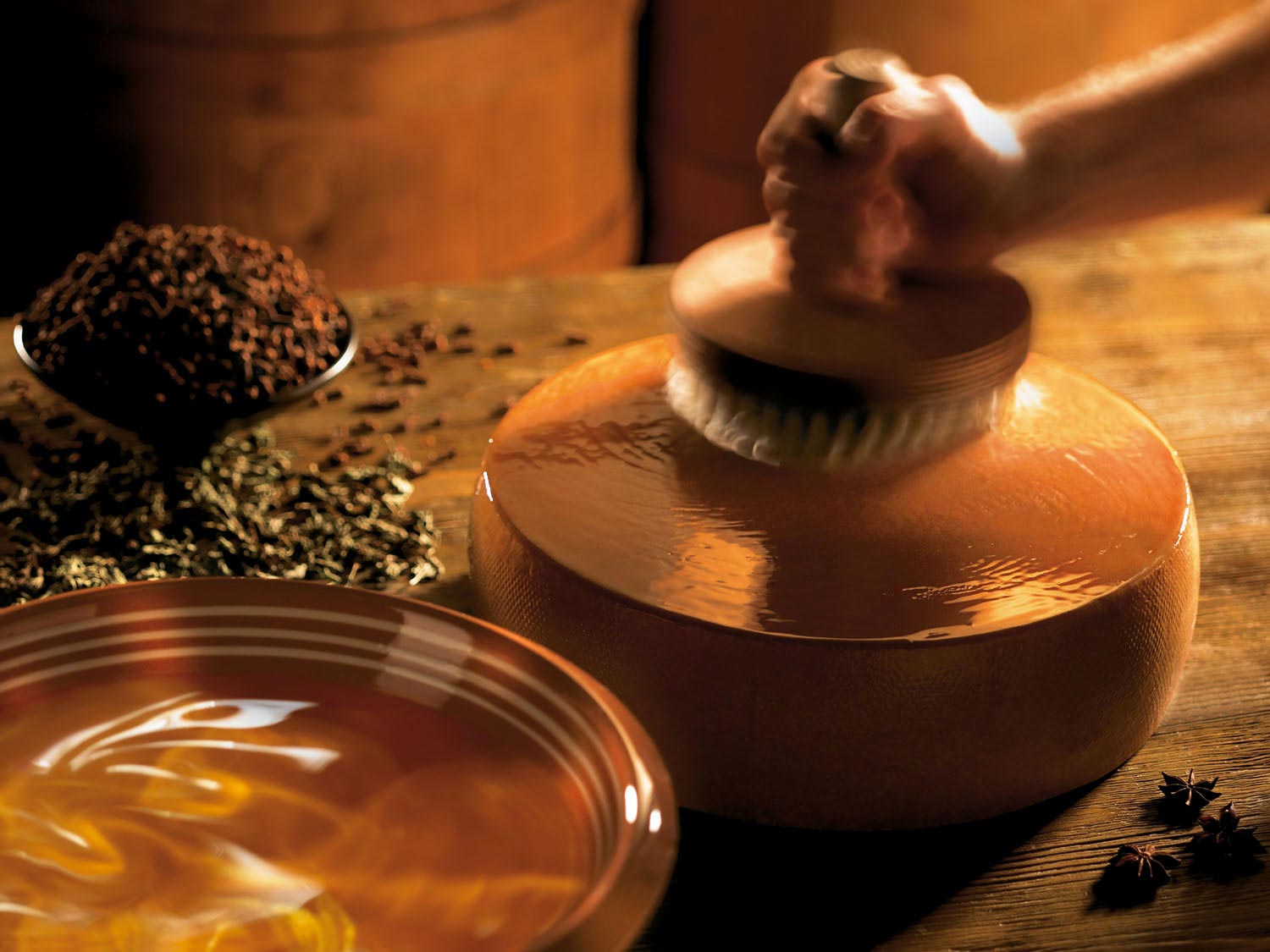 Handwerkliche Bearbeitung einer Keramikoberfläche mit einem Pinsel, um sie glatt zu machen. Im Hintergrund sind Gewürze und Tee sichtbar.