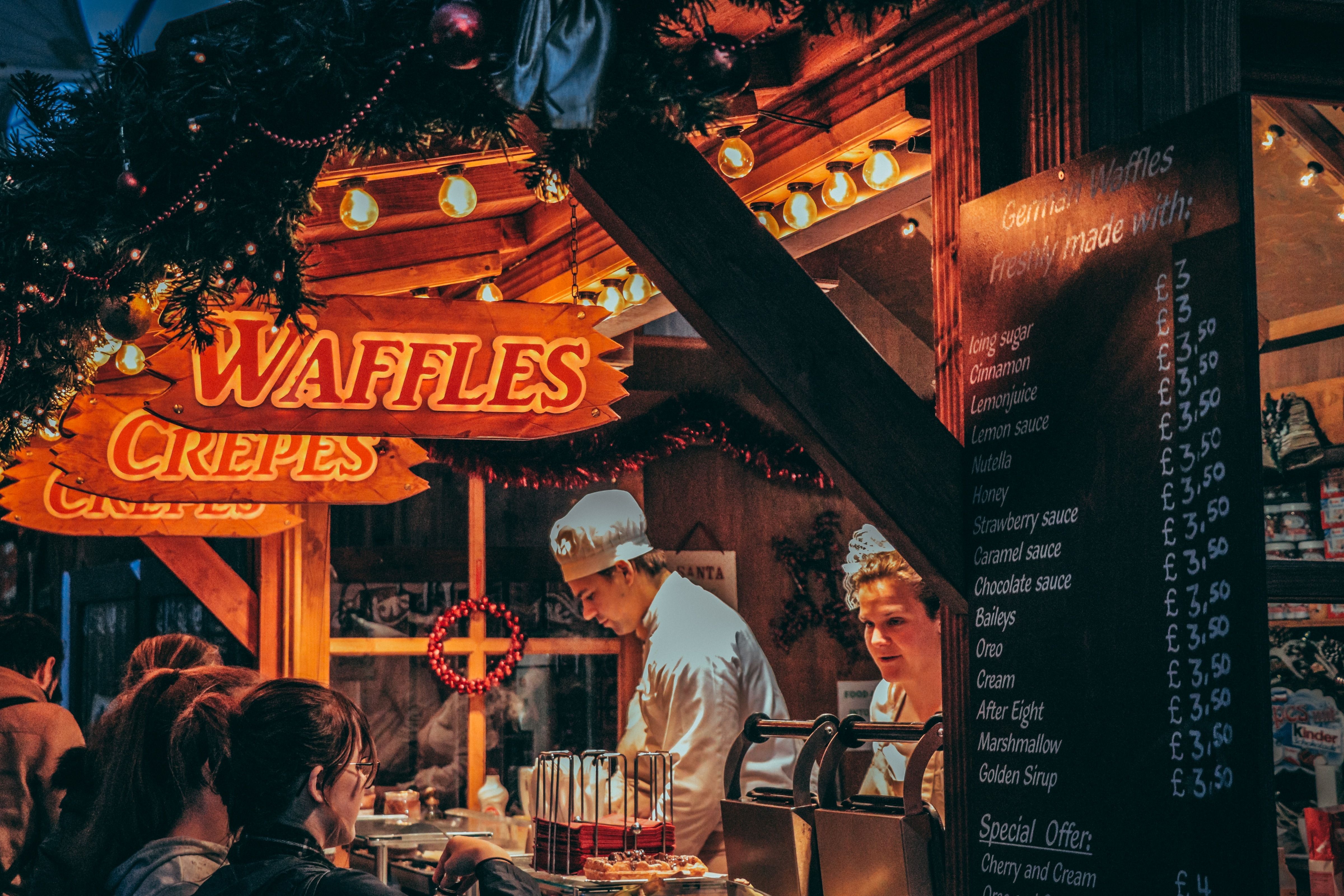 Weihnachtsmarkt: Waffel- und Crêpesstand mit festlicher Beleuchtung und fröhlichen Menschen.
