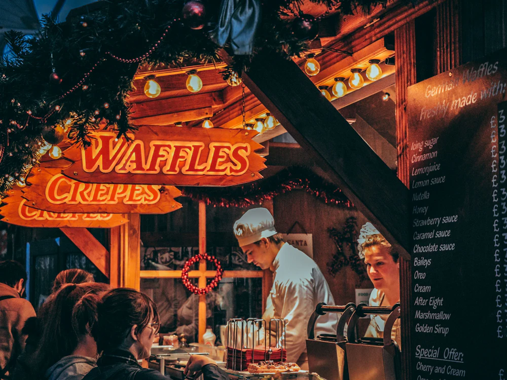 Weihnachtsmarkt: Waffel- und Crêpesstand mit festlicher Beleuchtung und fröhlichen Menschen.