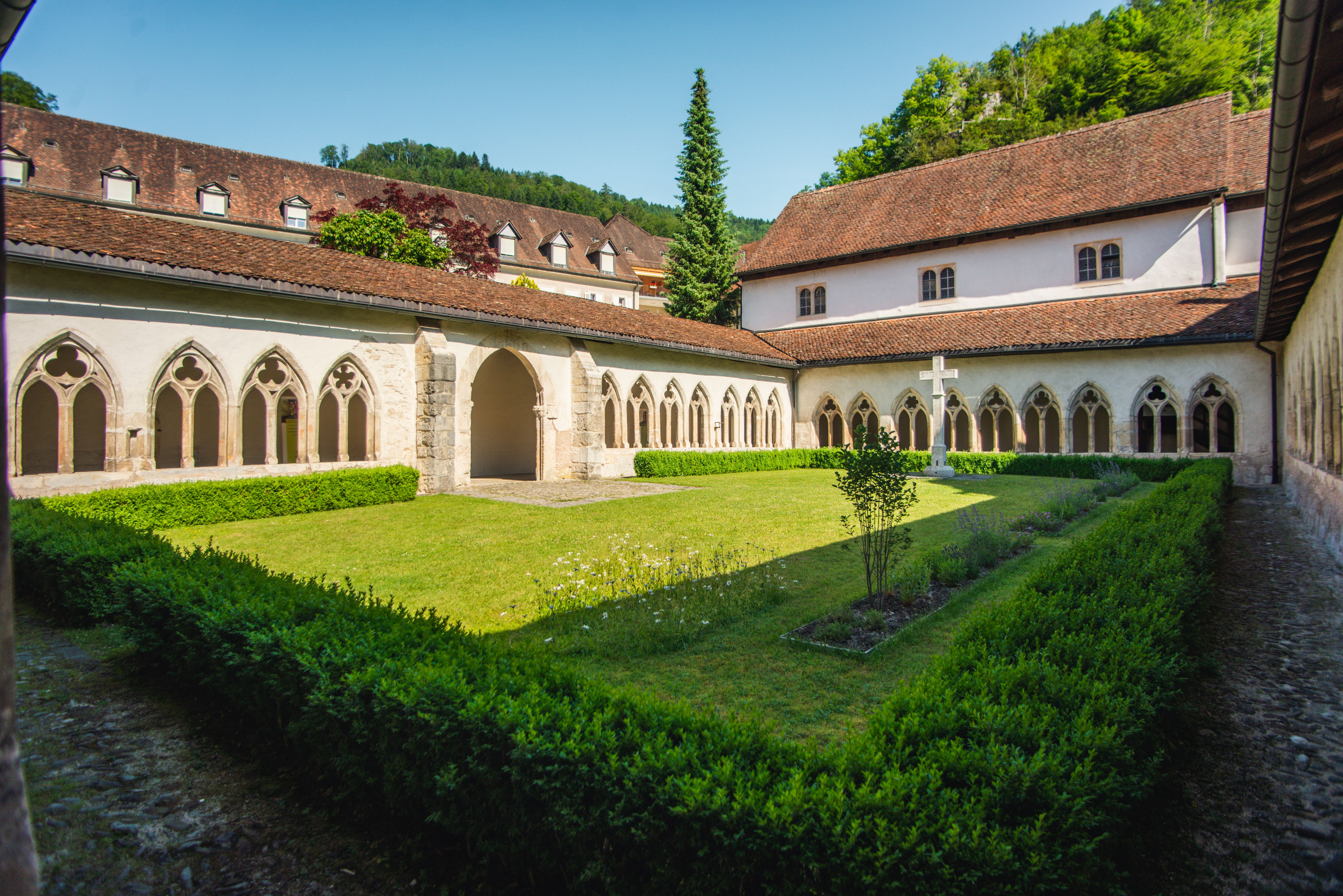 Circuit Secret Saint Ursanne: cloître tranquille avec des bâtiments historiques et une cour verte en ambiance estivale.
