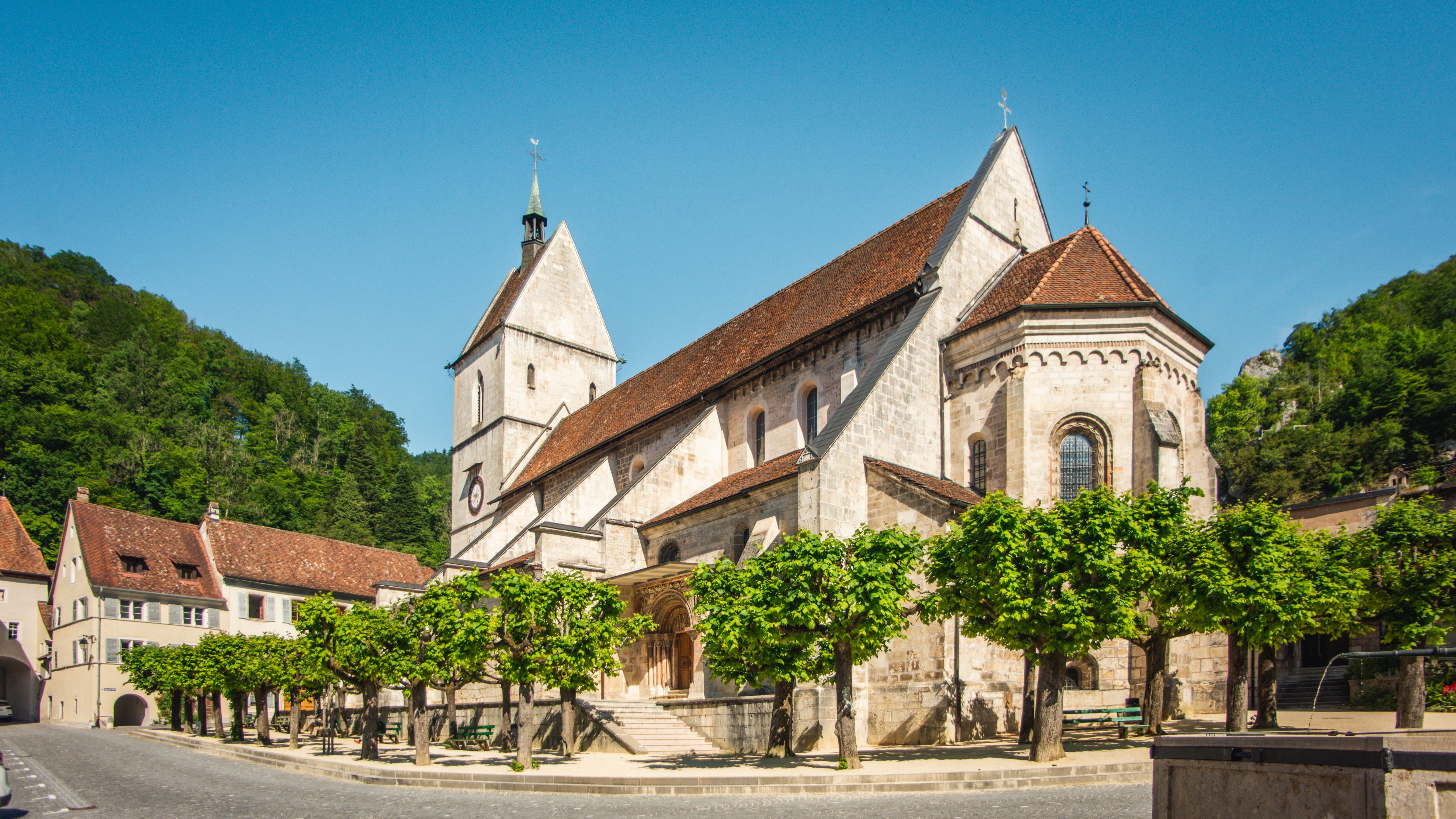 Circuit Secret Saint Ursanne : Église historique dans un cadre pittoresque avec de nombreux arbres et beaucoup de culture.