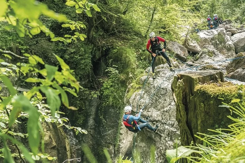 Canyoning Interlaken with group members rappelling down rocks in a green environment.