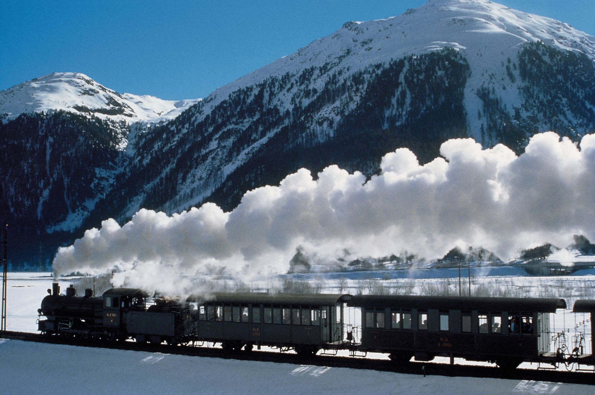 Engadin Round Trip Steam Experience Train travels through snow-covered landscape.