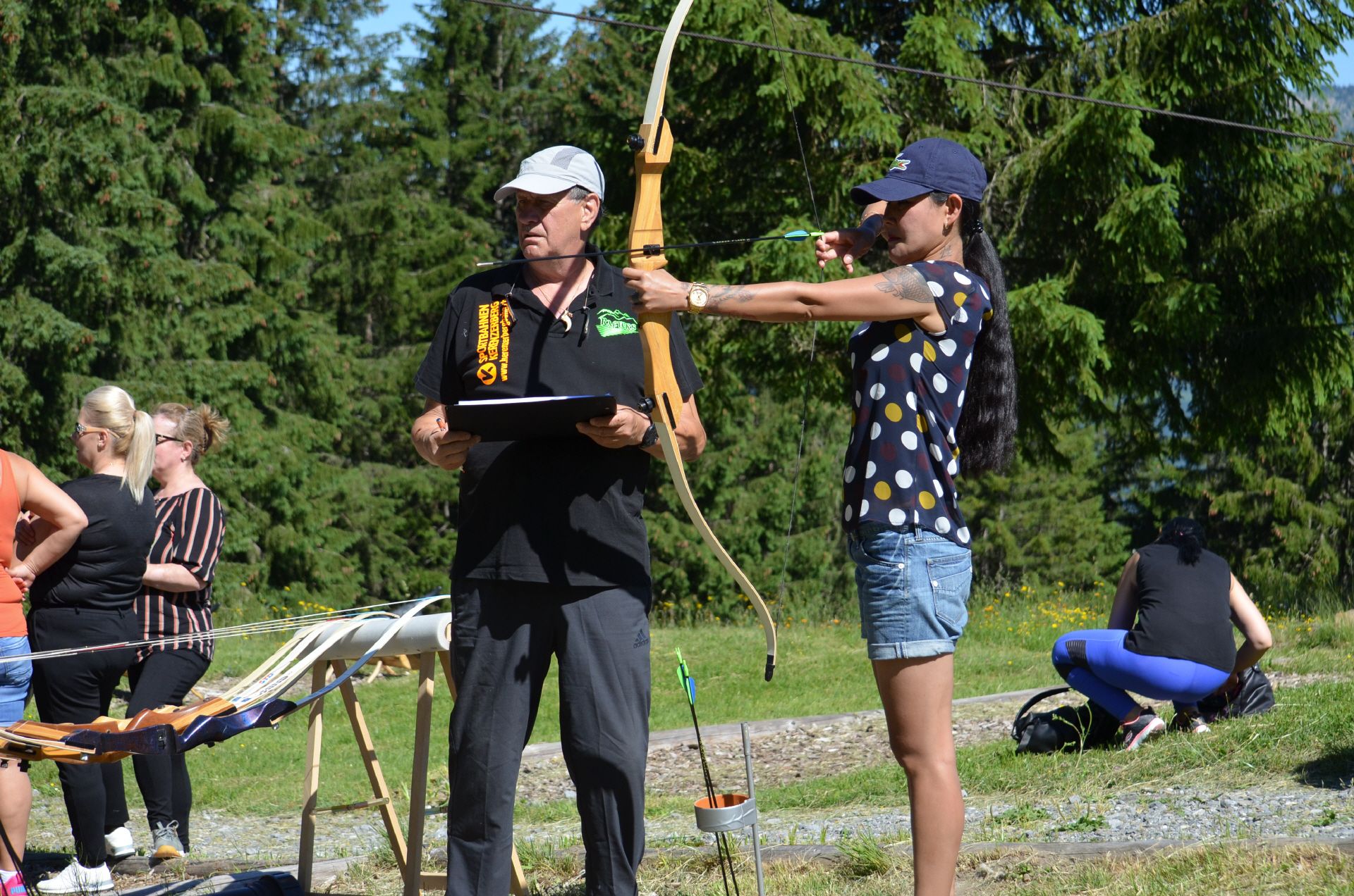 Швейцария стрельба из лука: инструктор по обучению, участница в спортивной одежде, зеленая окружающая среда