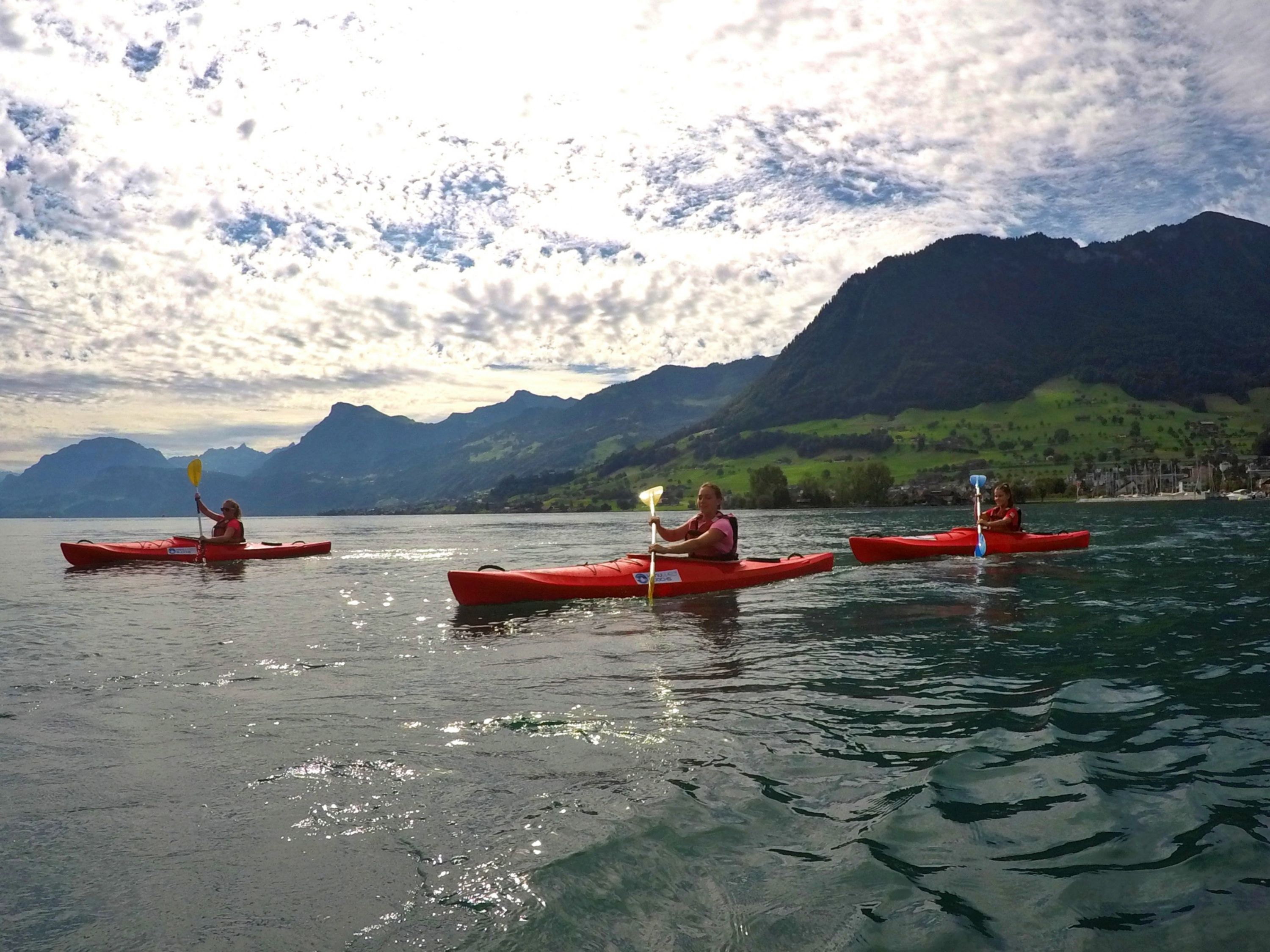 Sea kayak tour on Lake Lucerne with friends in red kayaks against a mountain backdrop.