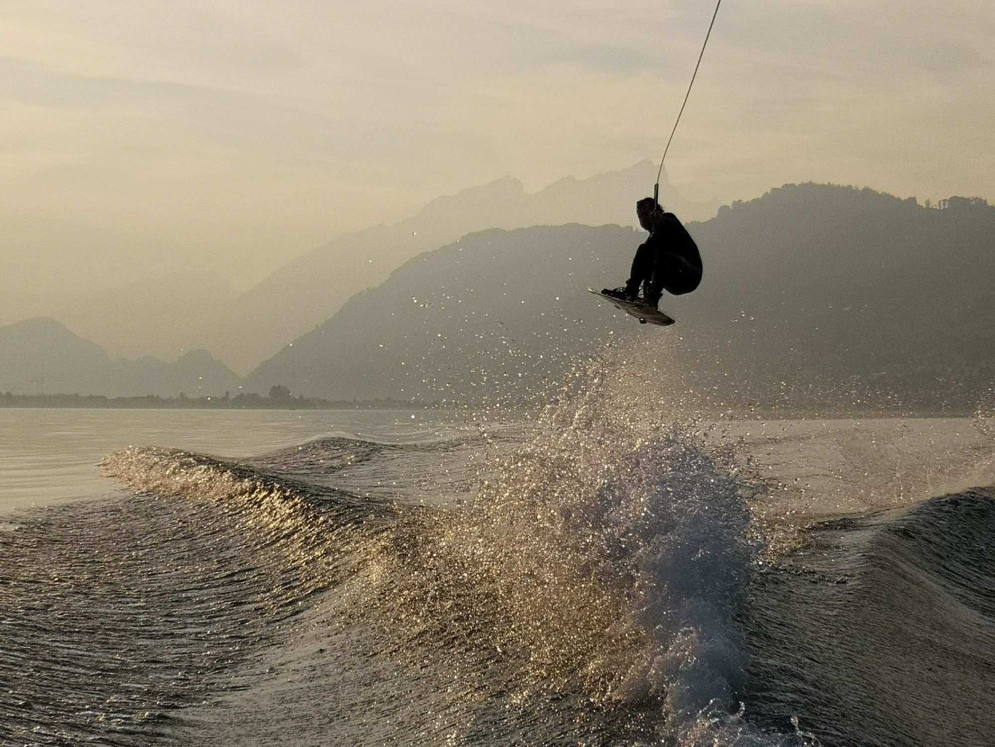 Wakeboarden: sporter springt over golven, adembenemend landschap en watersportplezier in de zomer.