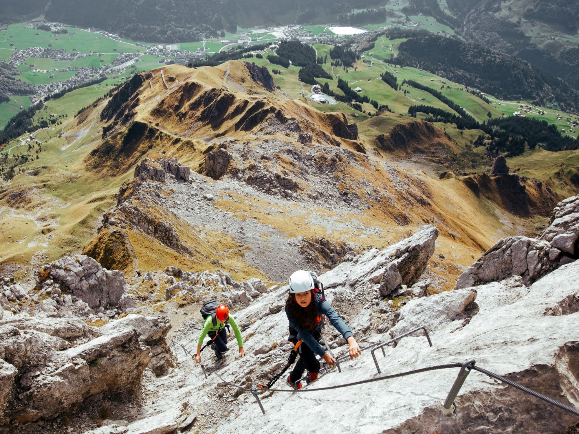 Via ferrata: two climbers on a vertical wall with Engelberg in the background, sporty and adventurous.