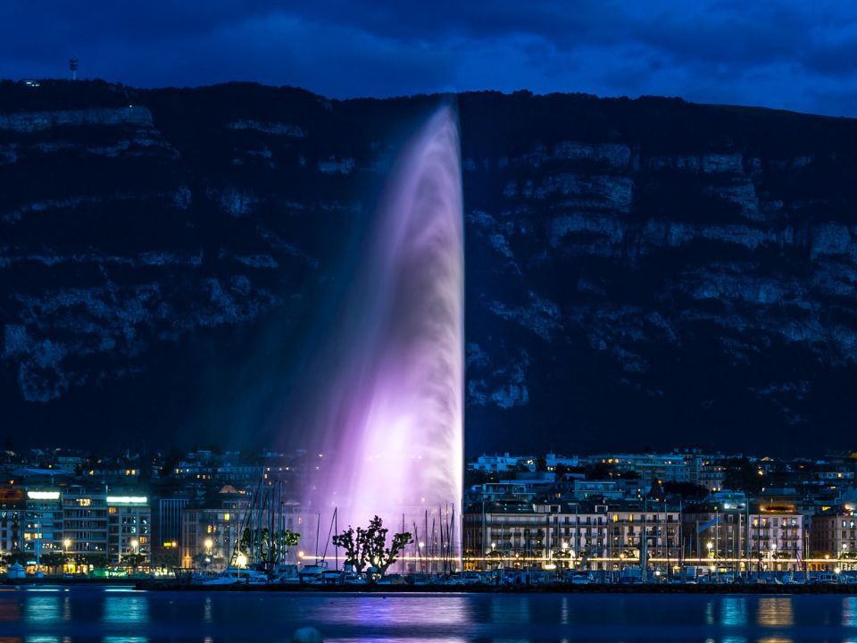 Fontanna Jet d'Eau w Genewie nocą z kolorowymi światłami i pięknym widokiem na miasto