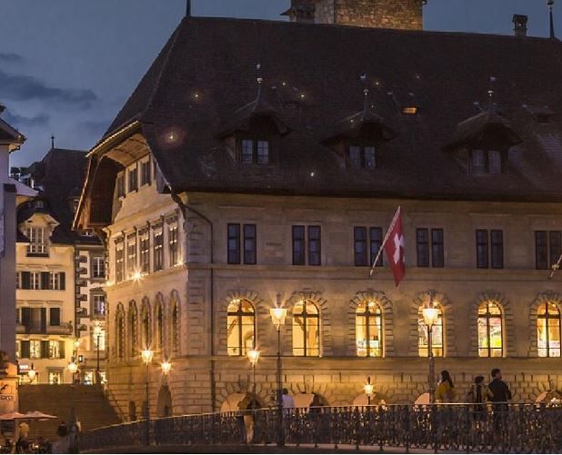 Hotel Hermitage Luzern, altes Gebäude bei Nacht, mit beleuchteten Fenstern und Schweizer Flagge.