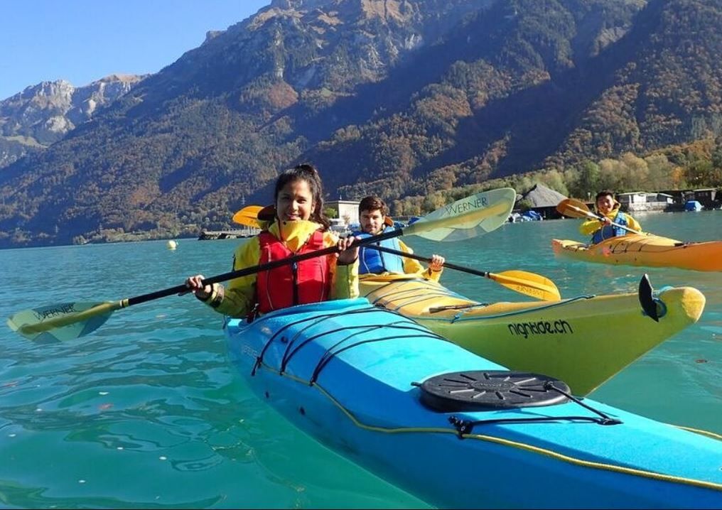 Kajakarstwo na Jeziorze Bienne. Dwoje kajakarzy w żółtych kajakach otoczonych górami. Czyste niebo i spokojna powierzchnia wody.