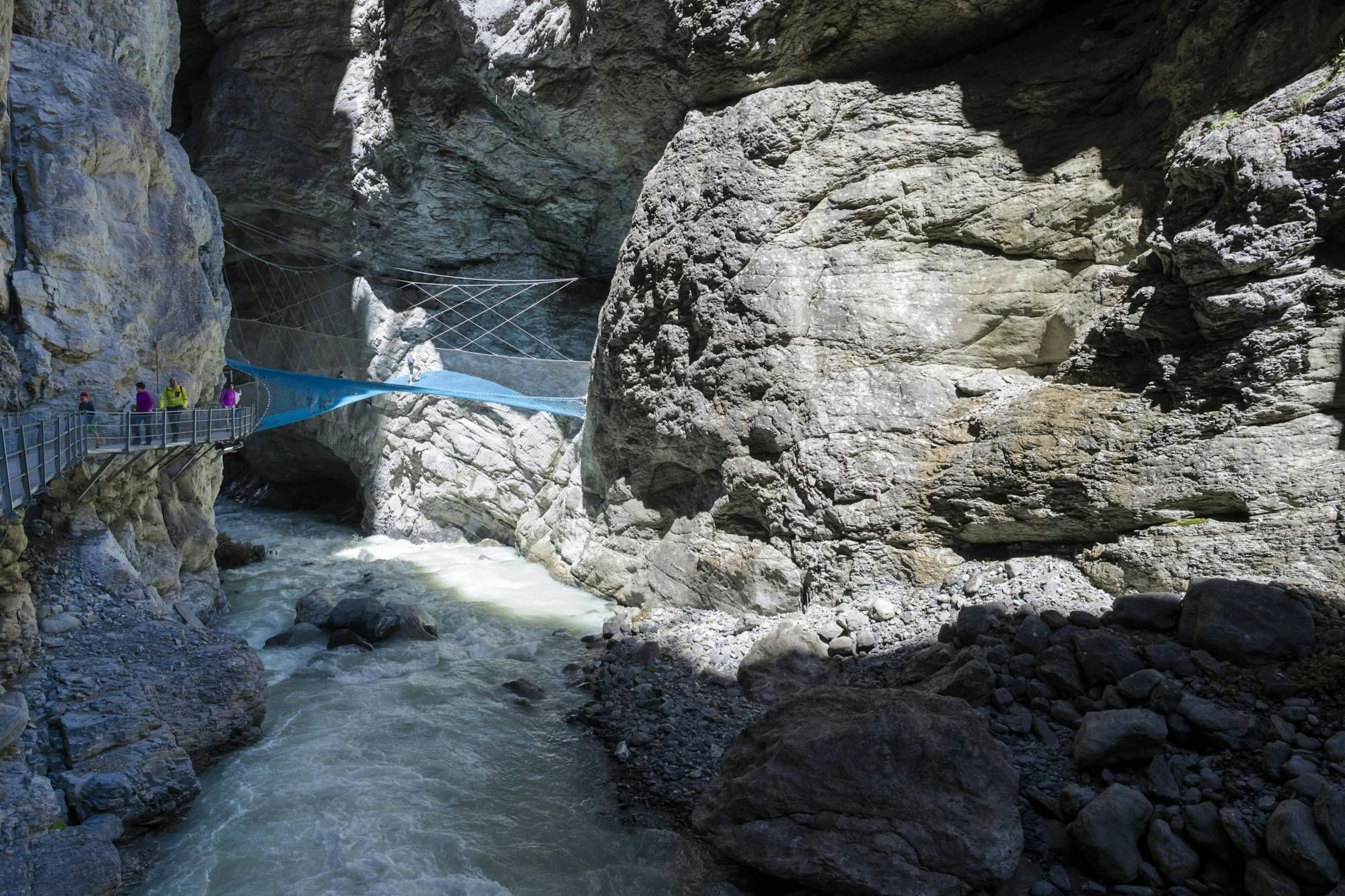 Ngarai glasier dengan jembatan dan sungai deras menampilkan batuan yang mengesankan.