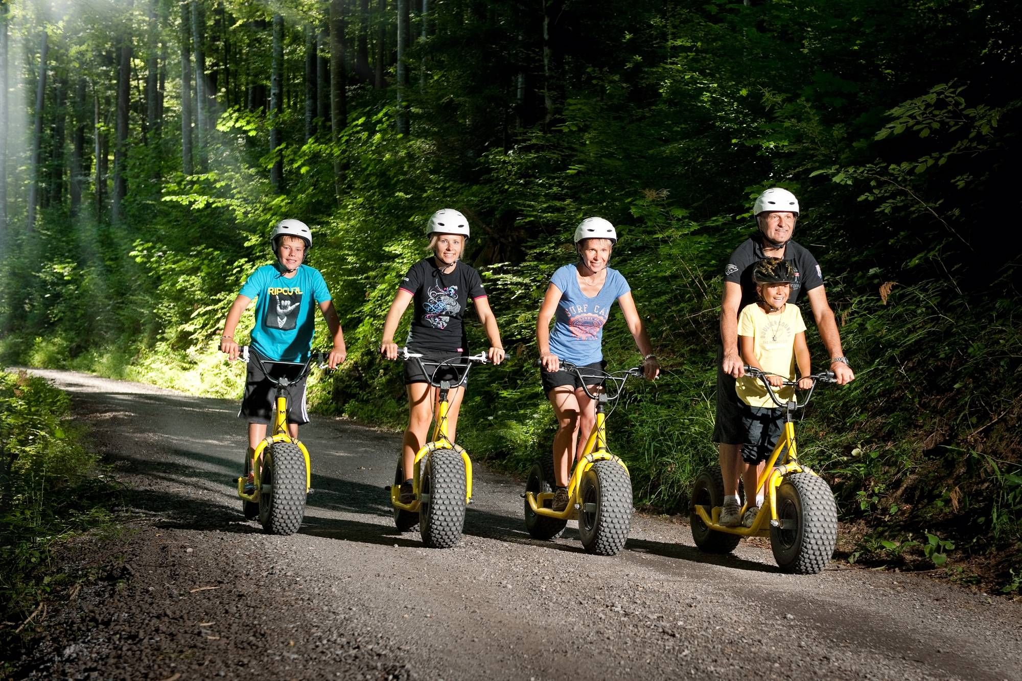 Family outing monster scooter on a forest path with four people and green surroundings.