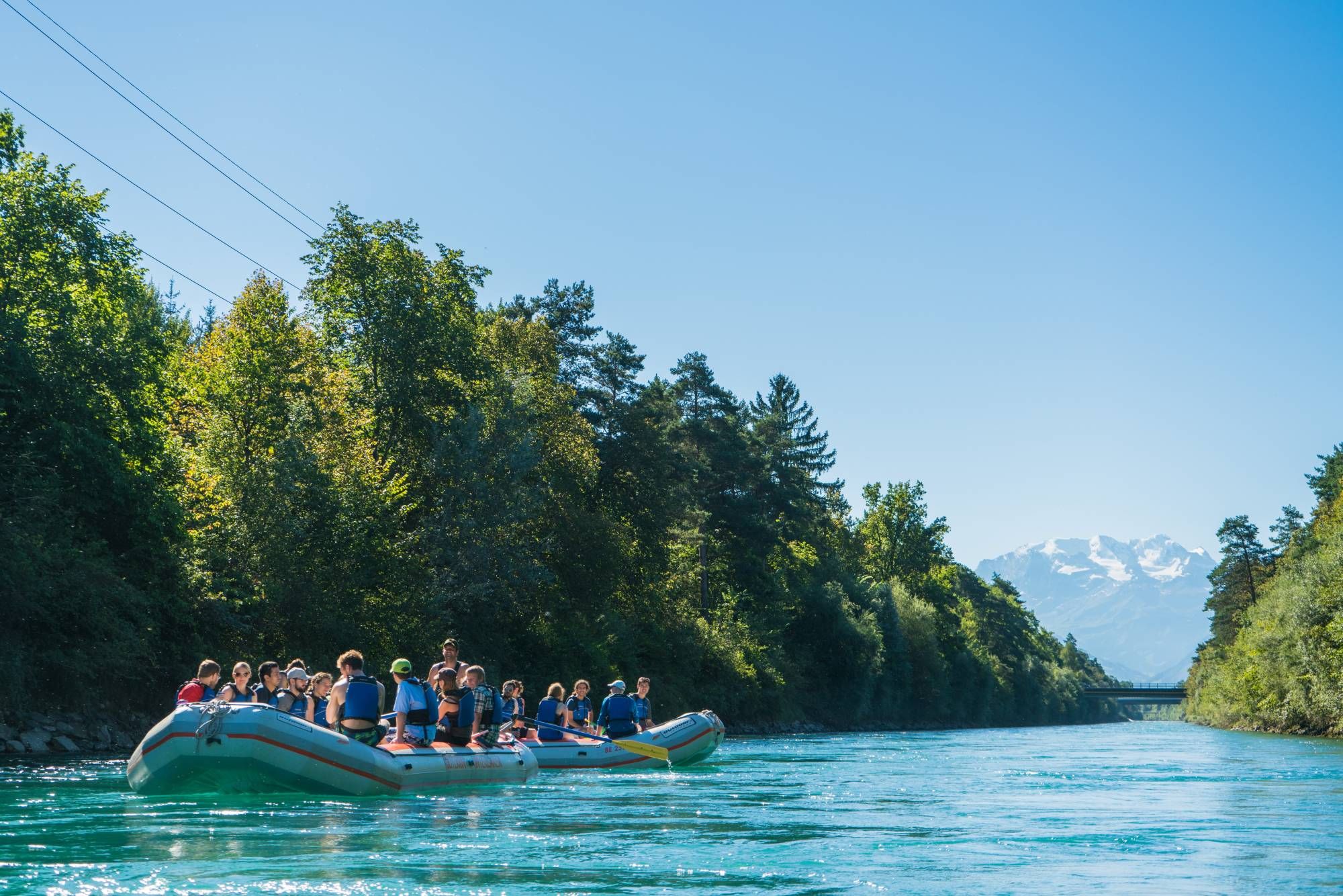 Raftingtour auf breitem Fluss mit Teilnehmern im Hintergrund.