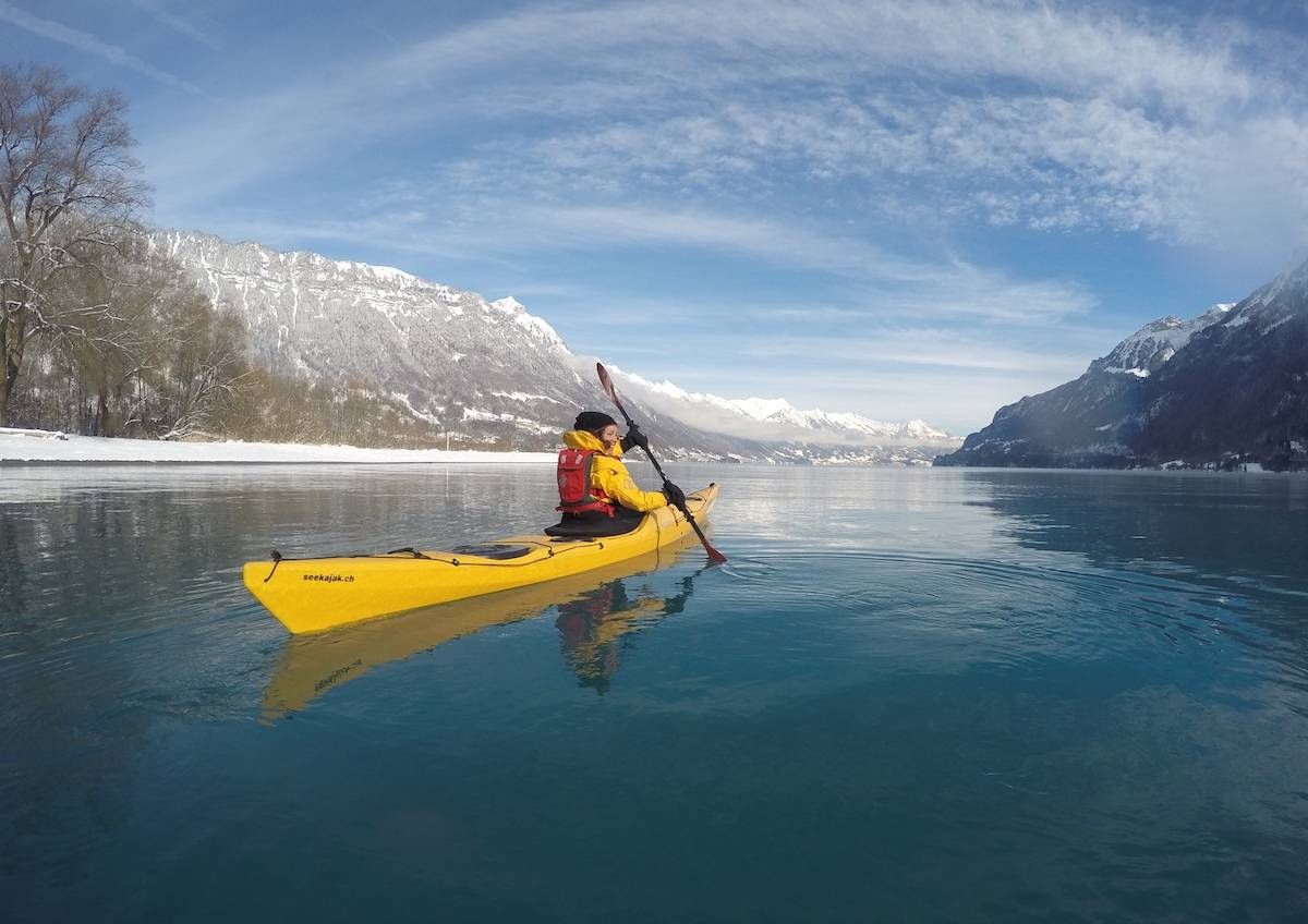 Kajakfahren am See im Winter, gelbes Kajak, Berge im Hintergrund