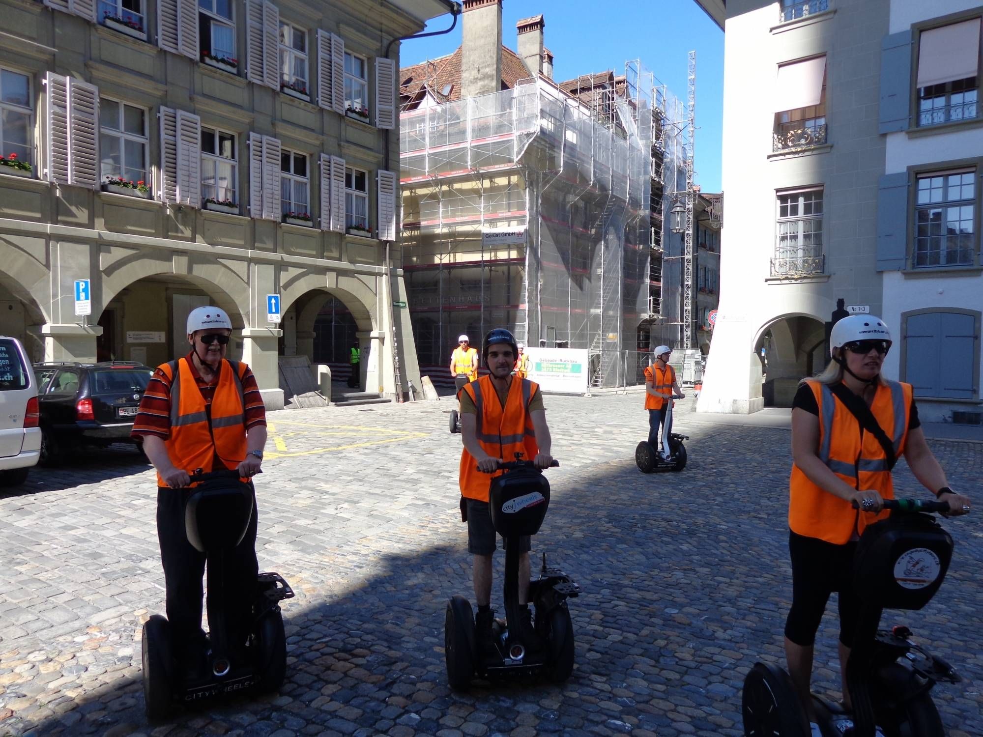 Segway Tour Bern mit Teilnehmern in orangefarbener Kleidung, historische Gebäude im Hintergrund.