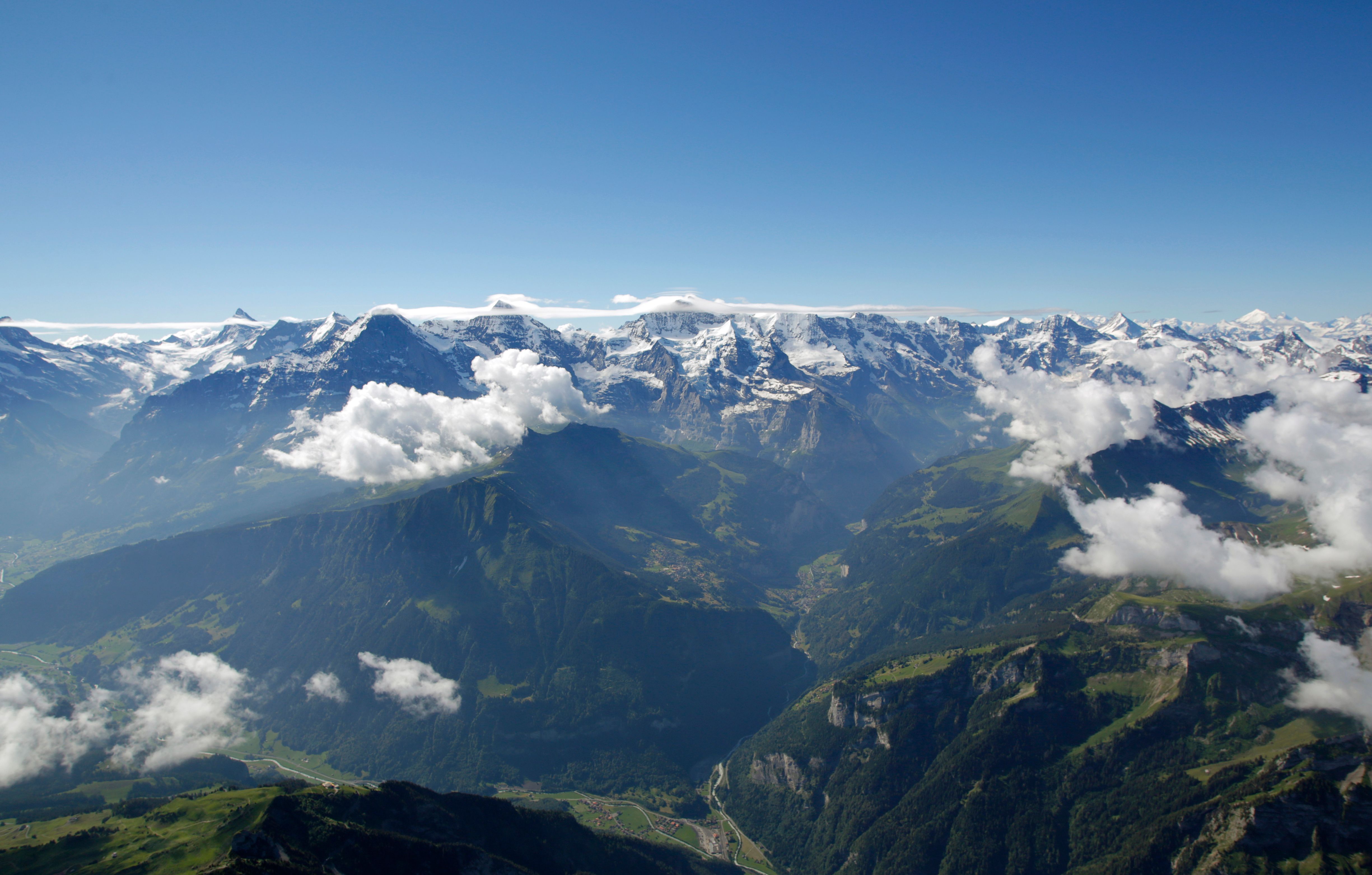 Alpflygning med helikopter över de schweiziska alperna, breda toppar och moln.