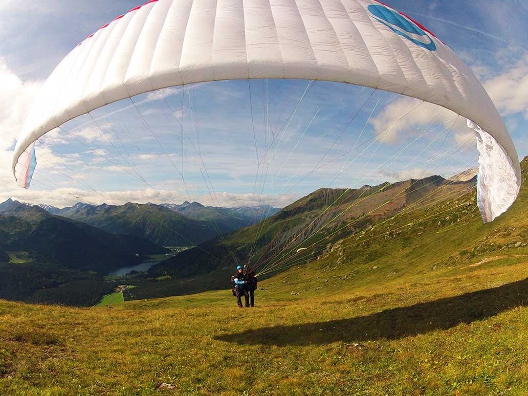 Paragliding ve dvojici v letní sezoně nad malebnou horskou krajinou v Davosu.
