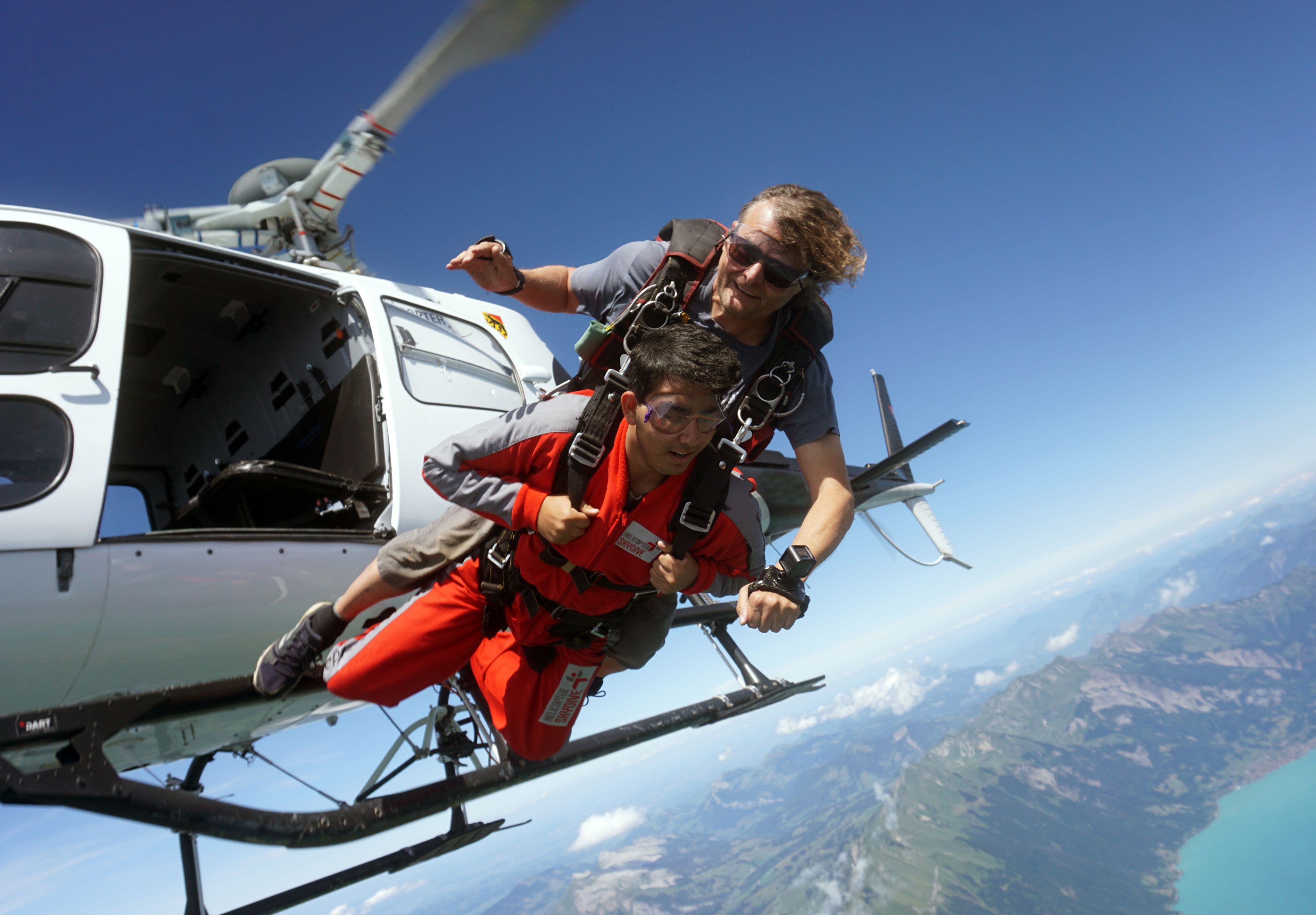 Skydiving from a helicopter over Bern with a blue sky and mountain panorama.