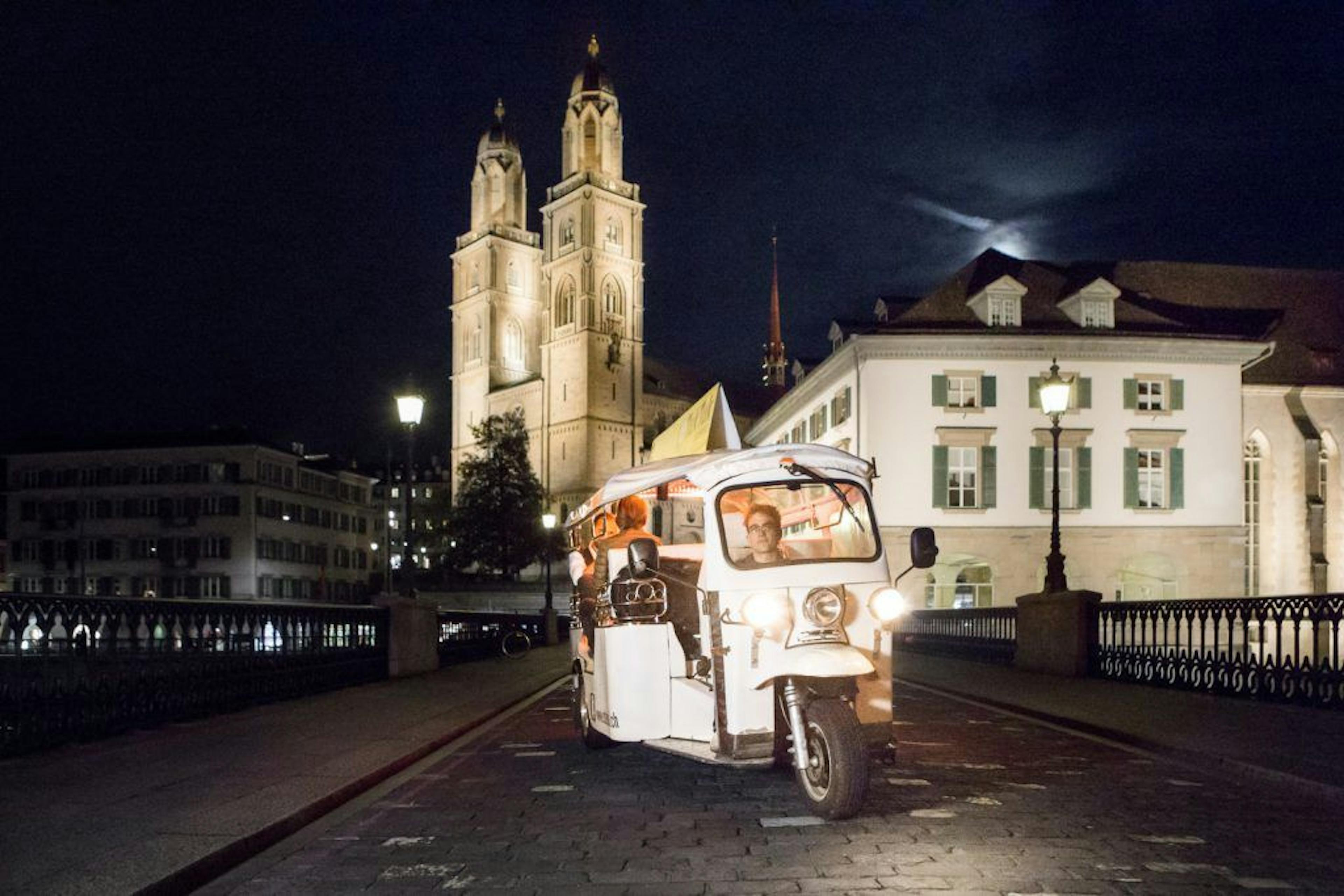 Zürich E-Tuk in notturna attraverso la città con sfondo illuminato