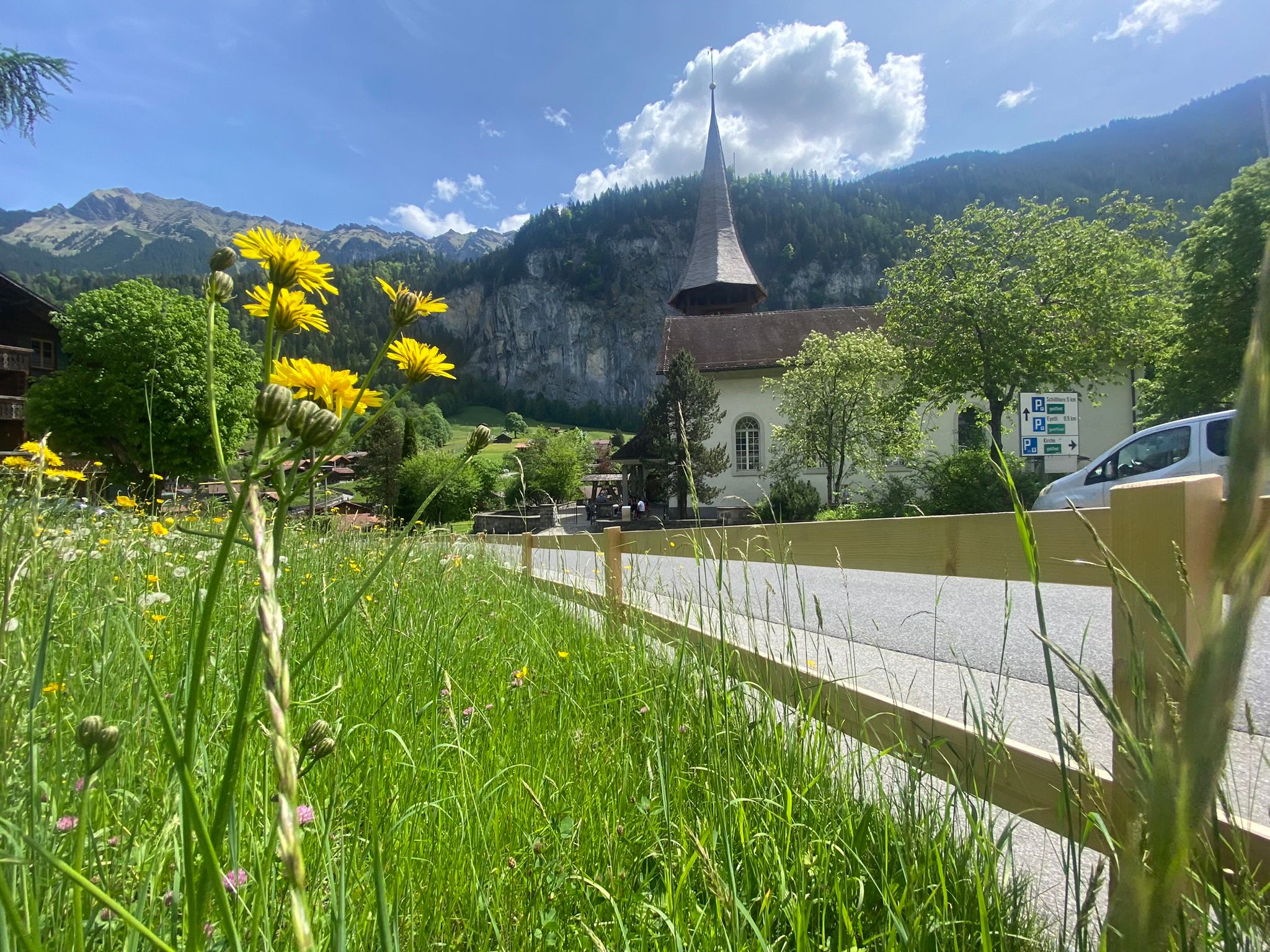 Lauterrunnen, virtuele reisbegeleiding met bloemen op de voorgrond, kerk en bergen op de achtergrond.