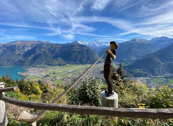 Virtual travel companion in Lauterbrunnen with a view of the mountains and a hiker. The sky is clear and the landscape is green.