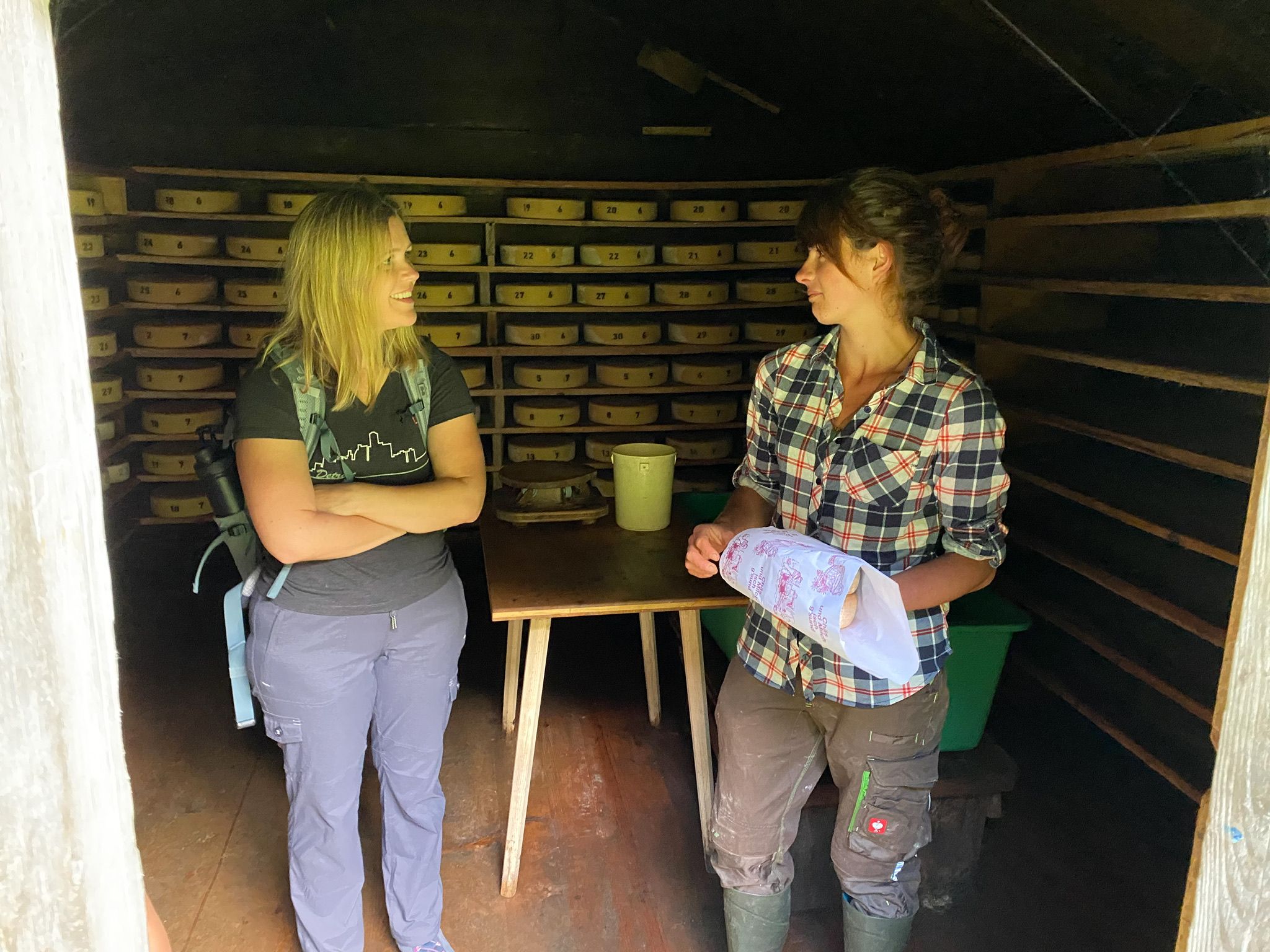 Two women discuss travel preparations in a wooden room.