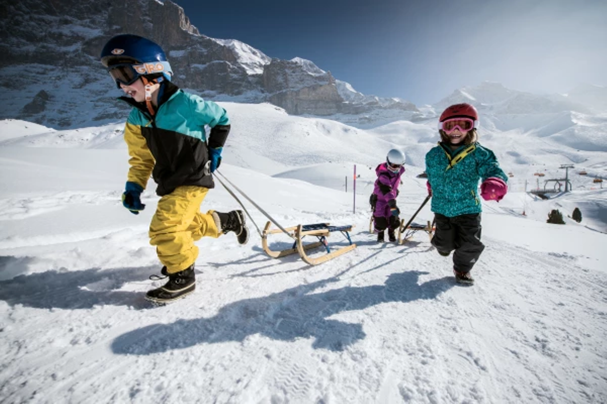 Skridskoåkning i Grindelwald: Barn åker pulka i snön, vinterglädje i bergen.