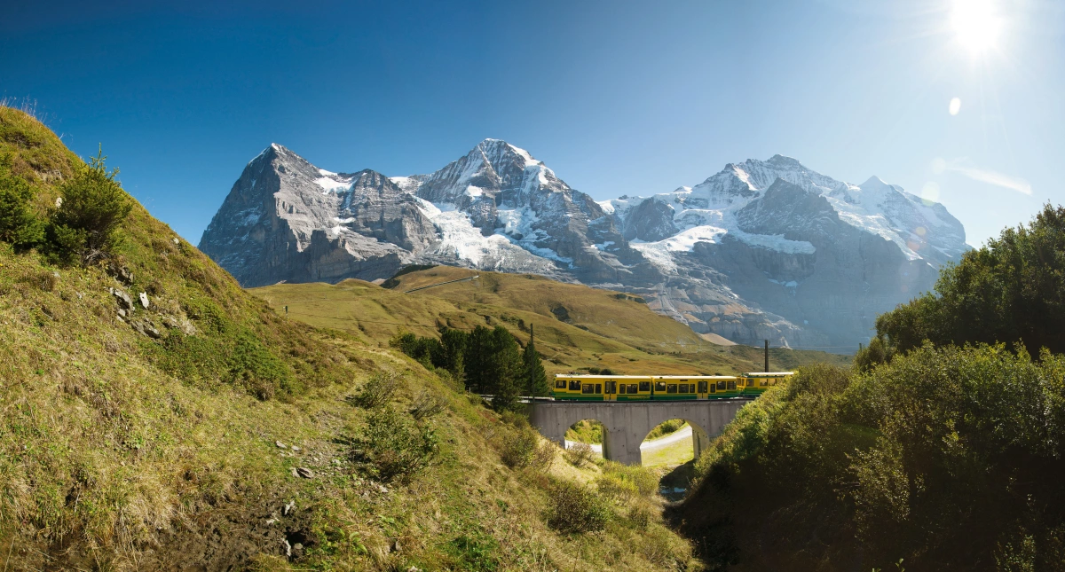 Kleine Scheidegg: Wengernalpbanen under Eiger med sommerlandskab og klar himmel.