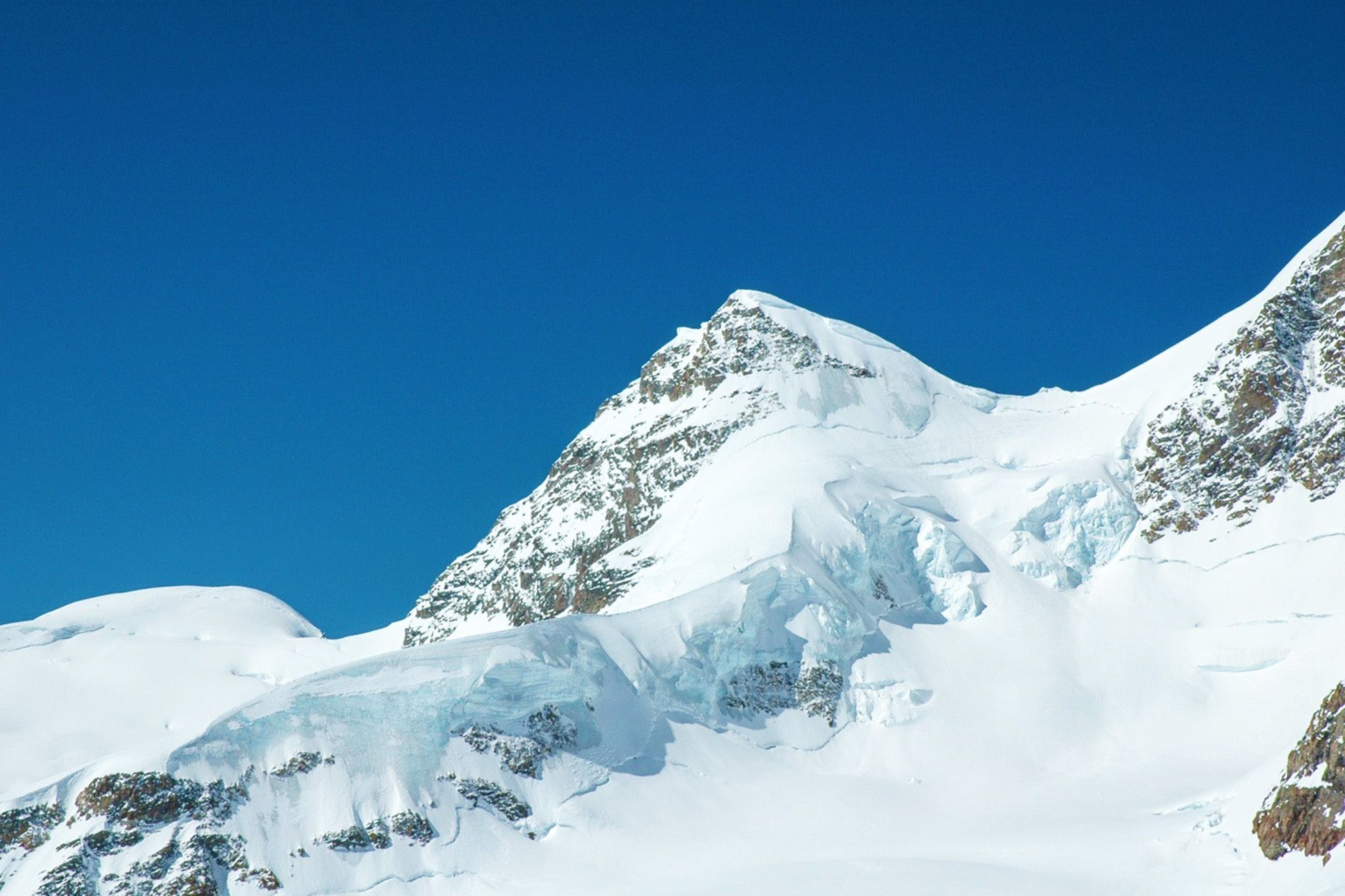 Jungfraujoch mit schneebedeckten Gipfeln und blauem Himmel.