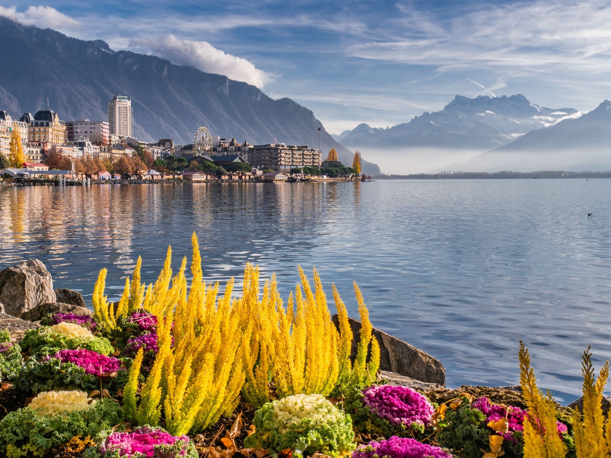 Montreux di tasik dengan bunga berwarna-warni dan gunung di latar belakang.